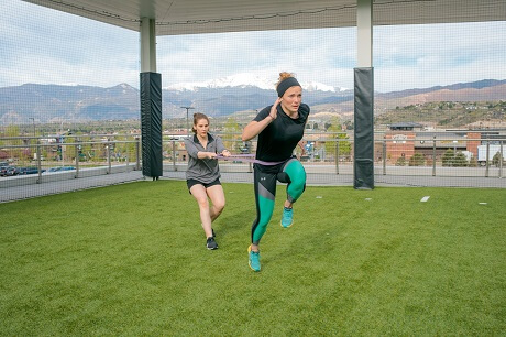 Two girls, one holds an elastic cord to the other's waist while she runs.